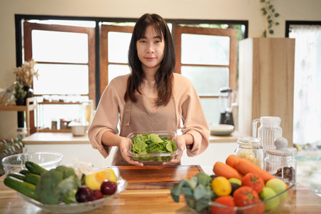 Young asian woman prepares fresh spinach in a cozy kitchen surrounded by vegetable and cooking...