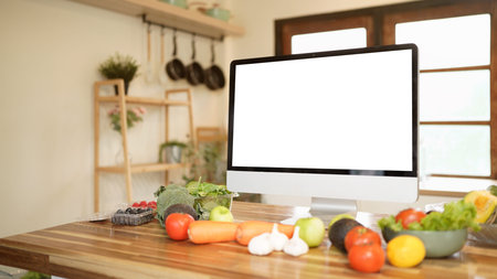 A mock up computer monitor with a blank screen sits on a wooden table with a variety of fruits and vegetables in front of it.の写真素材