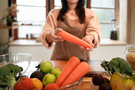 Portrait, woman and fresh carrots on kitchen table with organic produce, growth and vegetables in basket. Female person, happiness and nutrition for diet, healthy eating and sustainability in home.の写真素材