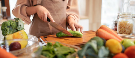 A woman is cutting cucumbers on a cutting board. The vegetables include carrots, broccoli