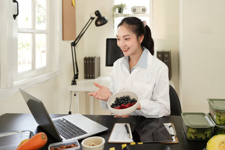 Female nutritionist having online consultation in office, preparing diet plan for patient, sitting...