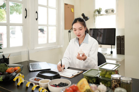 Healthcare professional, presumably a dietitian or nutritionist, with a clipboard in hand, writing notes in front of a table filled with various fresh vegetables.の写真素材