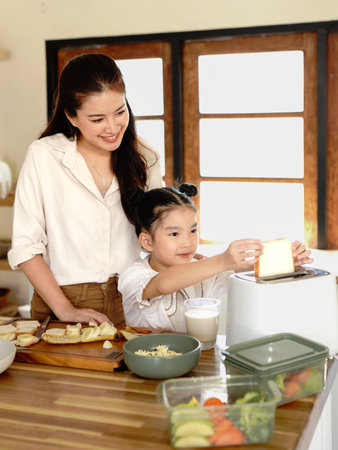 happy Mother teaching daughter making breakfast toast bread with toaster at home kitchen together . loving family. child girl excited looking Mom cooking indoors.の写真素材