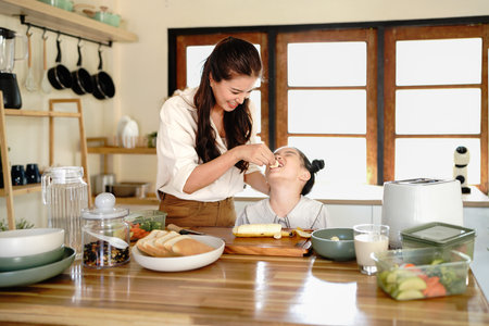 Mother and daughter preparing tasty food at kitchen, mom feeding kid daughter bananas in kitchen.の写真素材