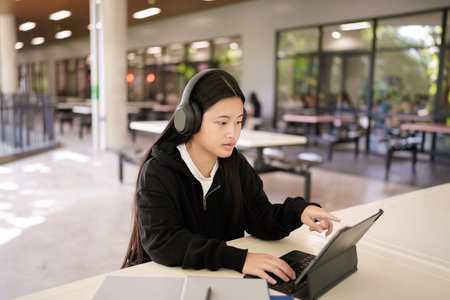 Teenage schoolgirl studying Wear headphones, using tablet , sitting in Library at school. Distance learning..の写真素材