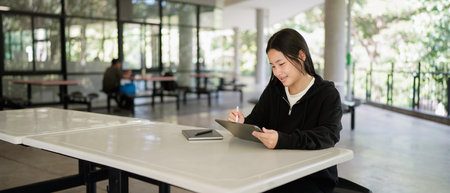 Asian high school student smiling while using a tablet while sitting outside the classroom.