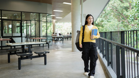 A young woman wearing a yellow sweater and carrying a backpack walks along a railing. She is looking up at the sky, possibly taking a break from her studies..の写真素材