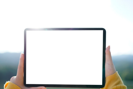 Woman hand holding a tablet with blank white screen with copy space. In the background blurred lake and sky. Remote work lifestyle and creative thinking in nature concept..の写真素材