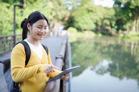 beautiful Asian girl student holding tablet and smiling at camera and learning and education concept on park in summer for relax time.の写真素材