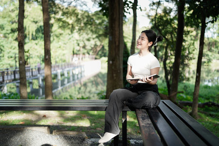 young teenage girl enjoying a quiet afternoon reading a book under a tree, with the sun filtering...