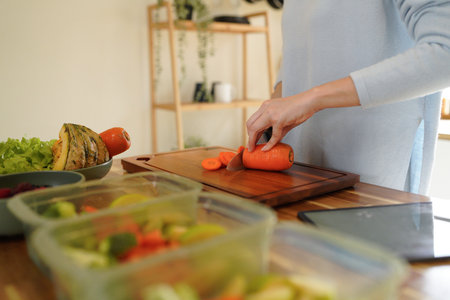 Woman cutting carrot near containers with fresh products on white marble table in kitchen, closeup. Food storage.の写真素材