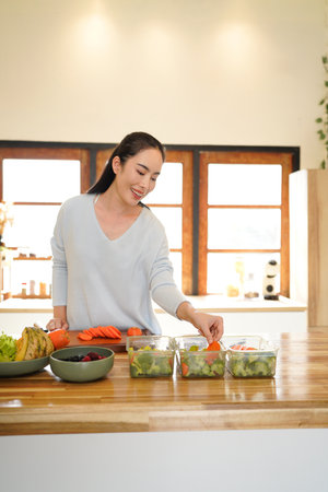 A woman preparing healthy meal prep in a bright kitchen with fresh vegetables and fruits.の写真素材