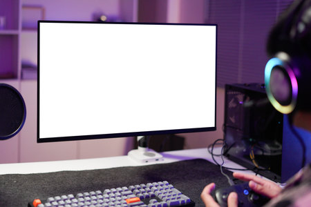 Man in dimly lit home playing video games on isolated screen gaming PC at computer desk, enjoying day off from work. Gamer battling enemies in online multiplayer shooter on mockup display.の写真素材