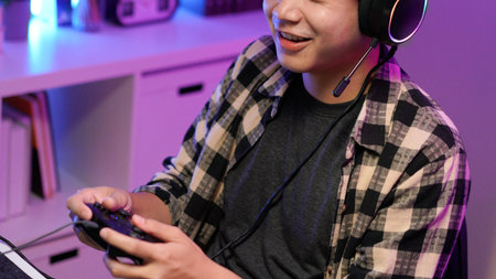 Attractive Asian male gamer enjoys playing online games on his computer feeling happy while live streaming a cyber tournament from home.の写真素材