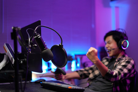 Happy asia guy gamer wear headphone participation play video game colorful neon lights computer in living room at night modern house. Esport streaming game online, Home quarantine activity concept..の写真素材
