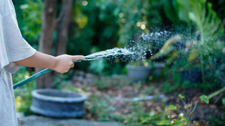 A hand holds a spray nozzle, watering plants in a garden.の写真素材