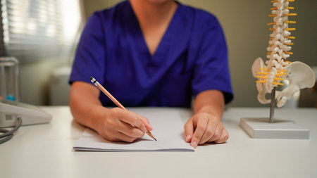 Doctor taking notes in office with spine model for diagnosis.の写真素材