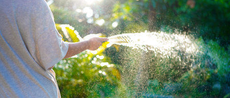 A hand holds a spray nozzle, watering plants in a garden.の写真素材