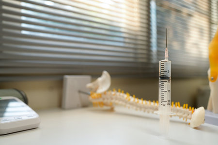 A syringe is on a table next to a model of a knee. The syringe is filled with a liquid and is ready to be used. Concept of preparation and anticipation for a medical procedure.の写真素材