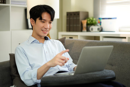 man freelancer working using laptop computer sitting on couch at home interior, guy surfing Internet, using modern technologies, free space.の写真素材