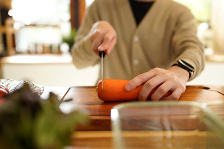A man is cutting a carrot on a wooden cutting board..の写真素材