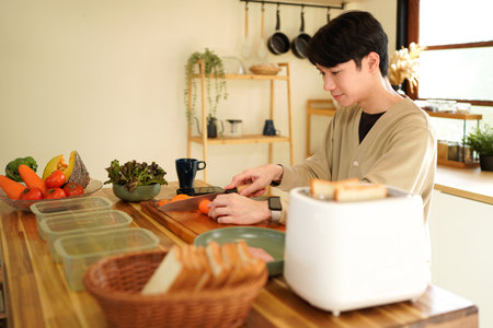 A man is cutting a carrot on a wooden cutting board..の写真素材