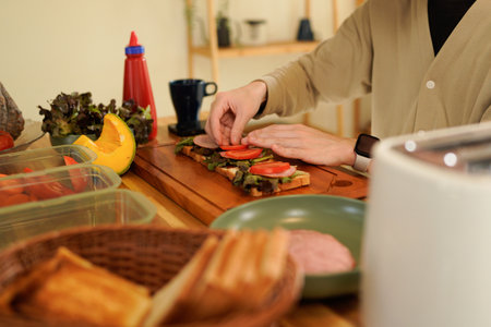 Man Making Sandwiches at bright and minimalist Counter with Fresh Greens, ham. Asian man cooking healthy foods in cozy kitchen in morning at home..の写真素材