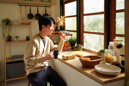 A man is eating a sandwich and drinking coffee Near the window in the morning. Scene is relaxed and casual.の写真素材
