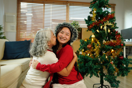 A joyful grandmother and granddaughter embrace joyfully in festive attire, surrounded by holiday decorations and a Christmas tree..の写真素材