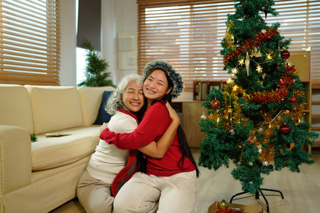 A joyful grandmother and granddaughter embrace joyfully in festive attire, surrounded by holiday decorations and a Christmas tree..の写真素材