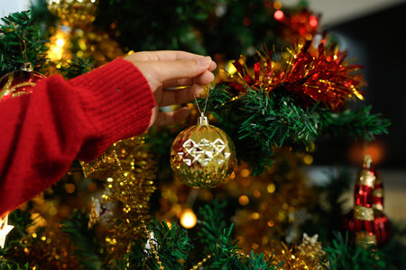 Hands decorating Christmas tree with ornaments and lights for festive holiday celebration.の写真素材