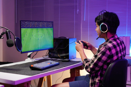 Attractive Asian male gamer enjoys playing online games on his computer feeling happy while live...