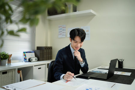 Asian business man in suit using laptop while sitting at his working place. Concentrated at work.の写真素材