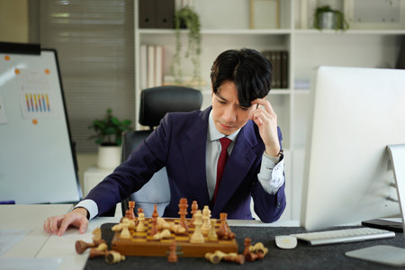 A man in a suit contemplates his next move in a chess game, showing concentration and strategic thinking..の写真素材