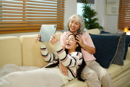 Smiling granddaughter and grandmother with tablet pc computer sitting on couch at home..