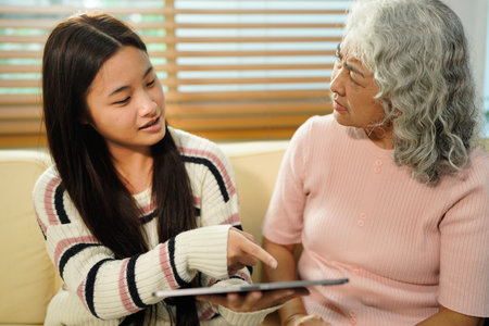grandmother and beautiful granddaughter in living room looking at the tablet. The granddaughter teaches her grandmother to use new technology.の写真素材