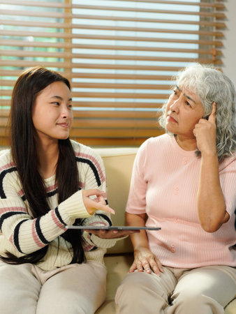 grandmother and beautiful granddaughter in living room looking at the tablet. The granddaughter teaches her grandmother to use new technology.の写真素材