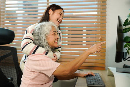 granddaughter teaches her grandmother work with computer at home.
