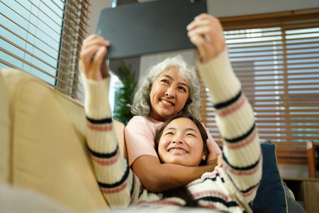 Smiling granddaughter and grandmother with tablet pc computer sitting on couch at home..の写真素材