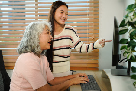 granddaughter teaches her grandmother work with computer at home.