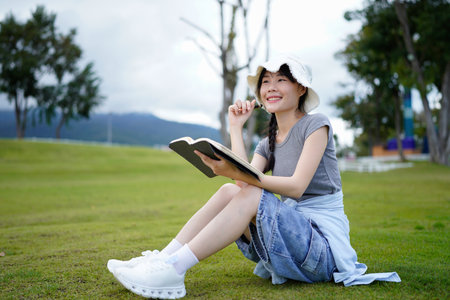 Photo of young attractive Asian woman writing on diary while sitting outdoors in the park, Writer sitting in garden, Female freelance are relaxing to writing story on jobs, beautiful Asian women.の写真素材