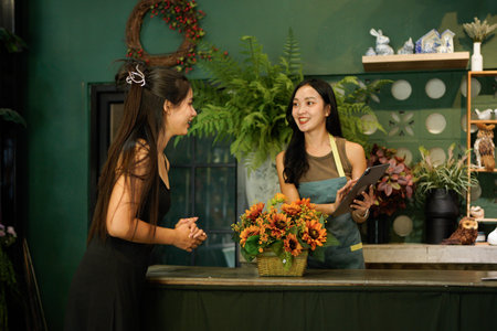 young florist girl Charge money on a tablet with female customer in flower shop, Deliver flower bouquets to customers.の写真素材