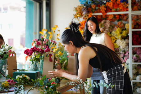 Asian woman is arranging flowers in a shop. There are other women working in the shop as well.の写真素材