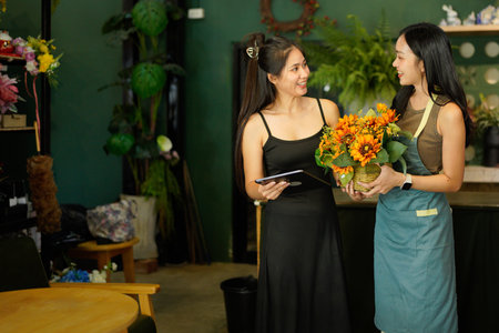 Waist up portrait of two young saleswomen using digital tablet for online orders while working in flower shop.の写真素材