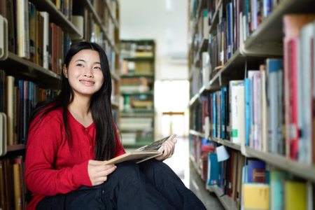asian teenage woman reading book in a library for education, studying and research in school,...