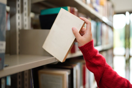 Female hand pulling book from bookshelf in public library in university, college or high school..