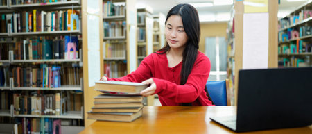 Female student with stack of books sitting at table in library.の写真素材