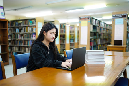 Young college woman working on his computer while studying in the library alone..