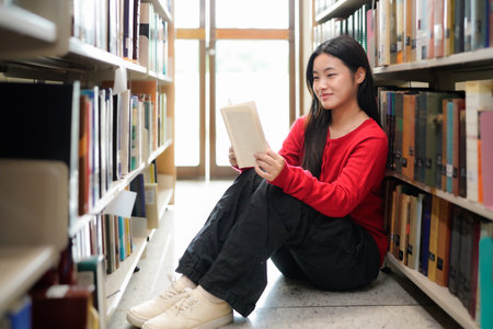 asian teenage woman reading book in a library for education, studying and research in school,...