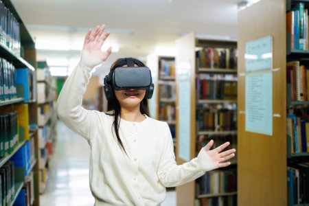 A woman wearing a white shirt is playing a video game with a virtual reality headset. She is standing in a library with shelves of books around herの写真素材